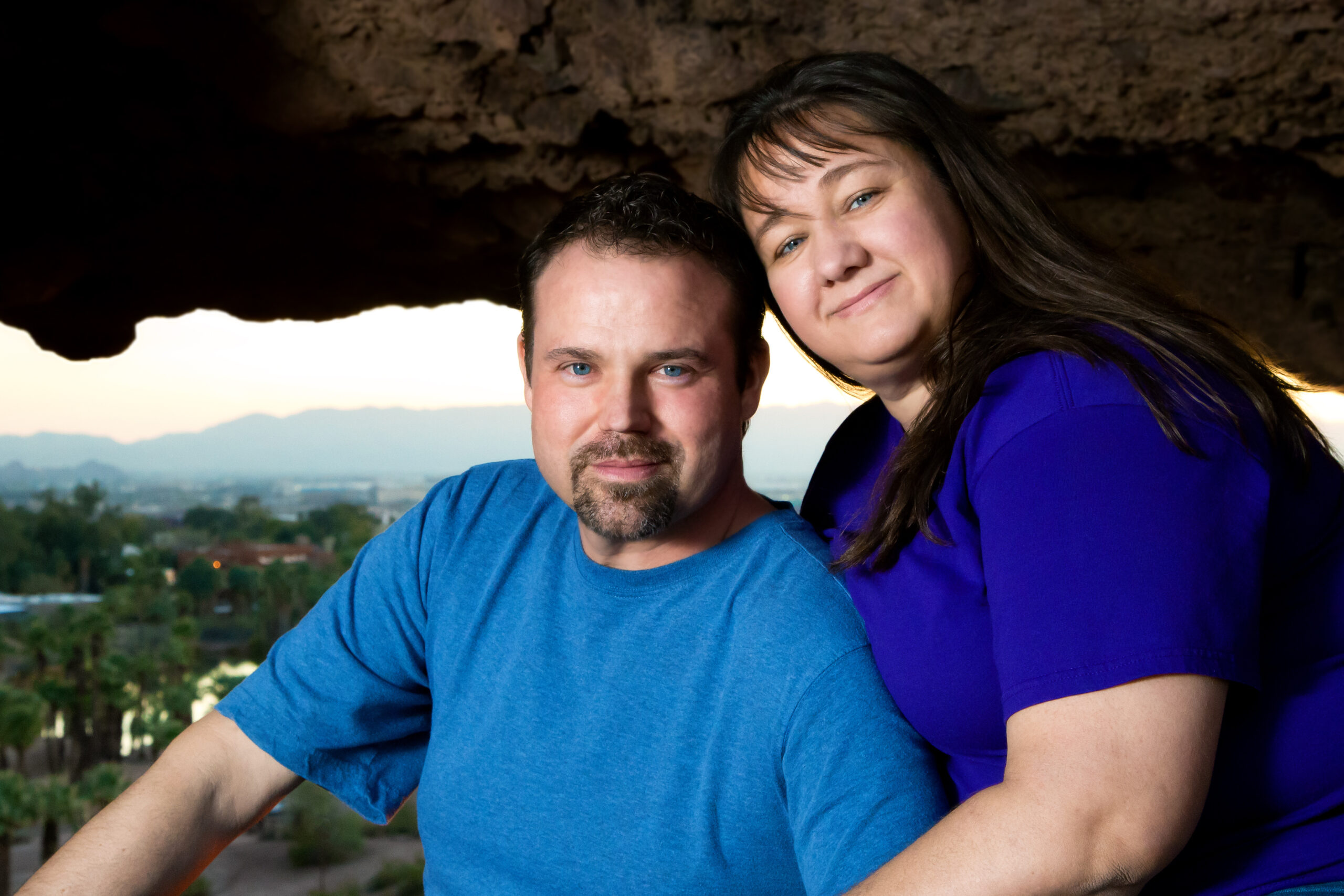 A blue eyed couple poses in a window hole of a rock overlooking the city of Phoenix, Arizona.